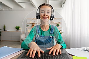 Girl sitting at desk, using laptop, wearing headset, typing