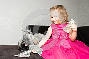 the girl is sitting on the edge of the sofa with her shih tzu dog and sharing money with her pet