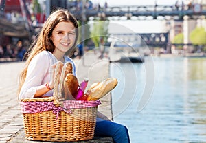 Girl sitting on embankment with picnic basket