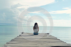 girl sitting at the end of a wooden pier, calm sea background