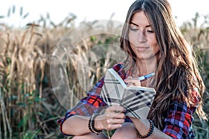 Girl sitting in a field shirt, wheat relaxing in nature, beautiful brunette hair. Keeps notepad pnany for the future