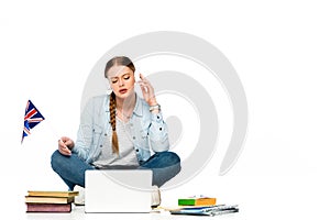 Girl sitting on floor in headphones near laptop, books and copybooks, holding uk flag