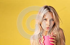 A girl sitting on the floor with her feet cross-legged keeps her head on a beautiful yellow background with a cup in