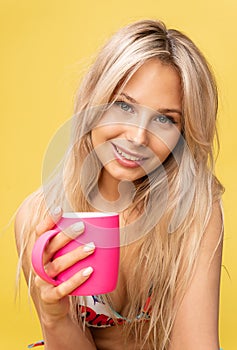 A girl sitting on the floor with her feet cross-legged keeps her head on a beautiful yellow background with a cup in