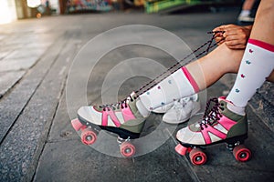 Girl is sitting on the floor and tying laces on her right roller. She is pulling them back. Also she put her right feet