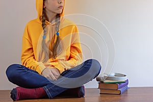 Girl sitting on the floor by the wall, wearing a yellow sweater with a hood over her head