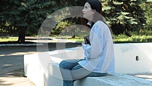 Girl sitting on the fountain in park, holds the book in his hands and dreaming.