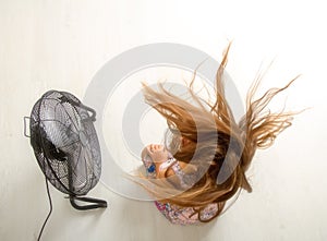 The girl is sitting in front of the fan