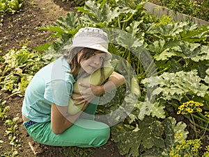 Girl sitting by the garden beds, picking a big zucchini