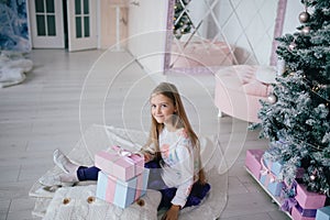 Girl sitting with gift boxes near Christmas tree at home