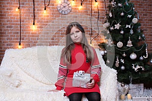 Girl sitting with a gift near the Christmas tree