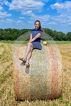 The girl is sitting on golden hay bales on the field