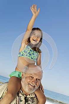 Girl Sitting On Grandfather's Shoulders At Beach