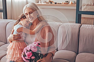 Girl sitting on the grandmothers laps holding bouquet of flowers at home