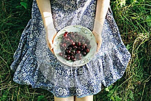 Girl is sitting on the grass in blue vintage dress. Woman is holding cherries. Rustic summer fruit flat lay. Healthy vegetarian