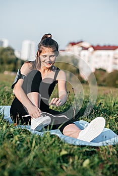 Girl sitting on grass with bottle and yoga mat. Fitness in the city metropolis on the grass in the summer outdoor