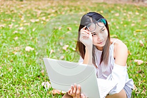 A girl sitting on the grass and hold labtop. She wear grasses.