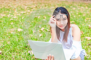 A girl sitting on the grass and hold labtop. She wear grasses.