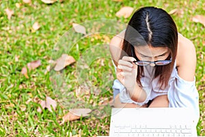 A girl sitting on the grass and hold labtop. She wear grasses.