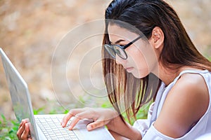 A girl sitting on the grass and hold labtop. She wear grasses.