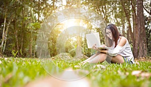 A girl sitting on the grass and hold labtop. She wear grasses.