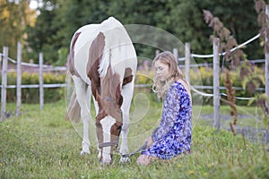 Girl sitting in the grass while a horse is grazing