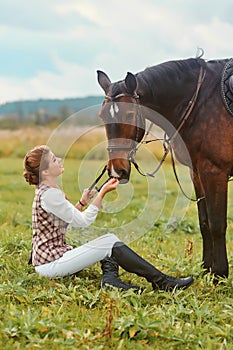 Girl sitting on the grass and stroking her horse