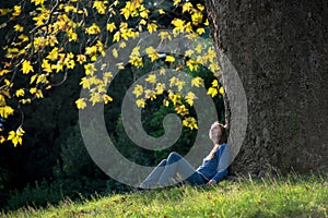 Girl sitting on the grass under a maple tree in autumn