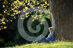 Girl sitting on the grass under maple tree in autumn