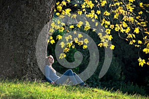 Girl sitting on the grass under maple tree in autumn