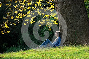 Girl sitting on the grass under maple tree in autumn