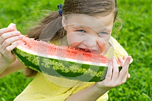 Girl sitting on green grass and eating a slice of juicy red watermelon