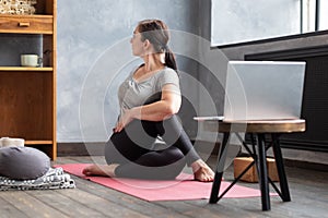 Girl sitting in Half lord of the fishes, Ardha Matsyendrasana pose at home.