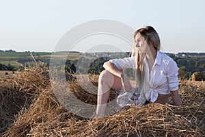 A girl is sitting in a haystack on the backdrop of the rural landscape