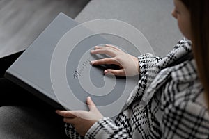 The girl is sitting, holding a gray leather photo book with an imprint of a memory in her hands