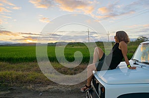 girl sitting on the hood of a car watching the sunset