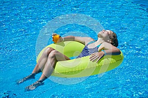 Girl sitting in inflatable ring in swimming pool with cold drink