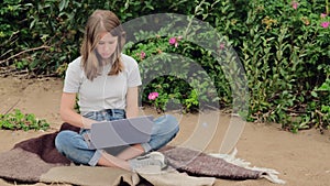 A girl is sitting by the lake watching in the laptop, concept of working outdoors, mostly blue and green colours.