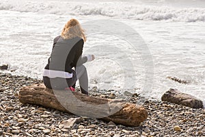 Girl sitting on log on the coast and looks at sea