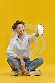 Girl sitting in lotos pose, showing smartphone.