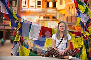 Girl sitting in the Lotus position on Buddhist stupa, prayer flags flying