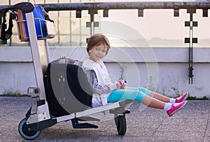 Girl sitting on luggage trolley waiting for flight by plane. Girk, kid at the airport