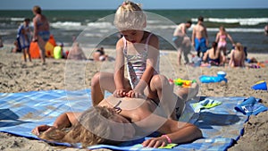 Girl sitting and massaging mother back on beach. Funny daughter do mom massage