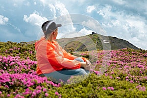 The girl is sitting on the meadow of the Carpathians with rhododendrons.
