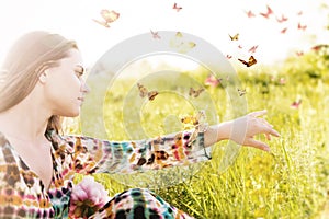 Girl sitting in a meadow in a swarm of flitting butterflies.