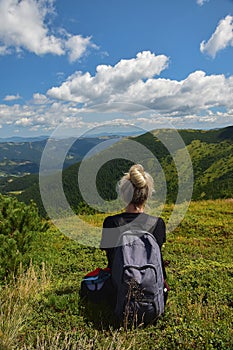 Girl sitting on a mountain top in summer with a backpack