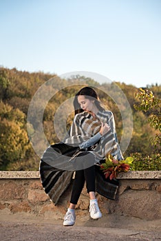 Girl sitting on nature background in blanket of autumn leaves in her hands. Vertical frame