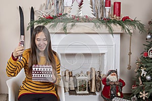 Girl is sitting near fireplace and christmas tree with gift