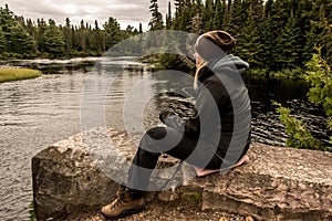 Girl sitting near Lake of two rivers in Algonquin National Park Canada Ontario natural pinetree landscape