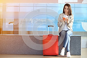Girl sitting near red suitcase in airport